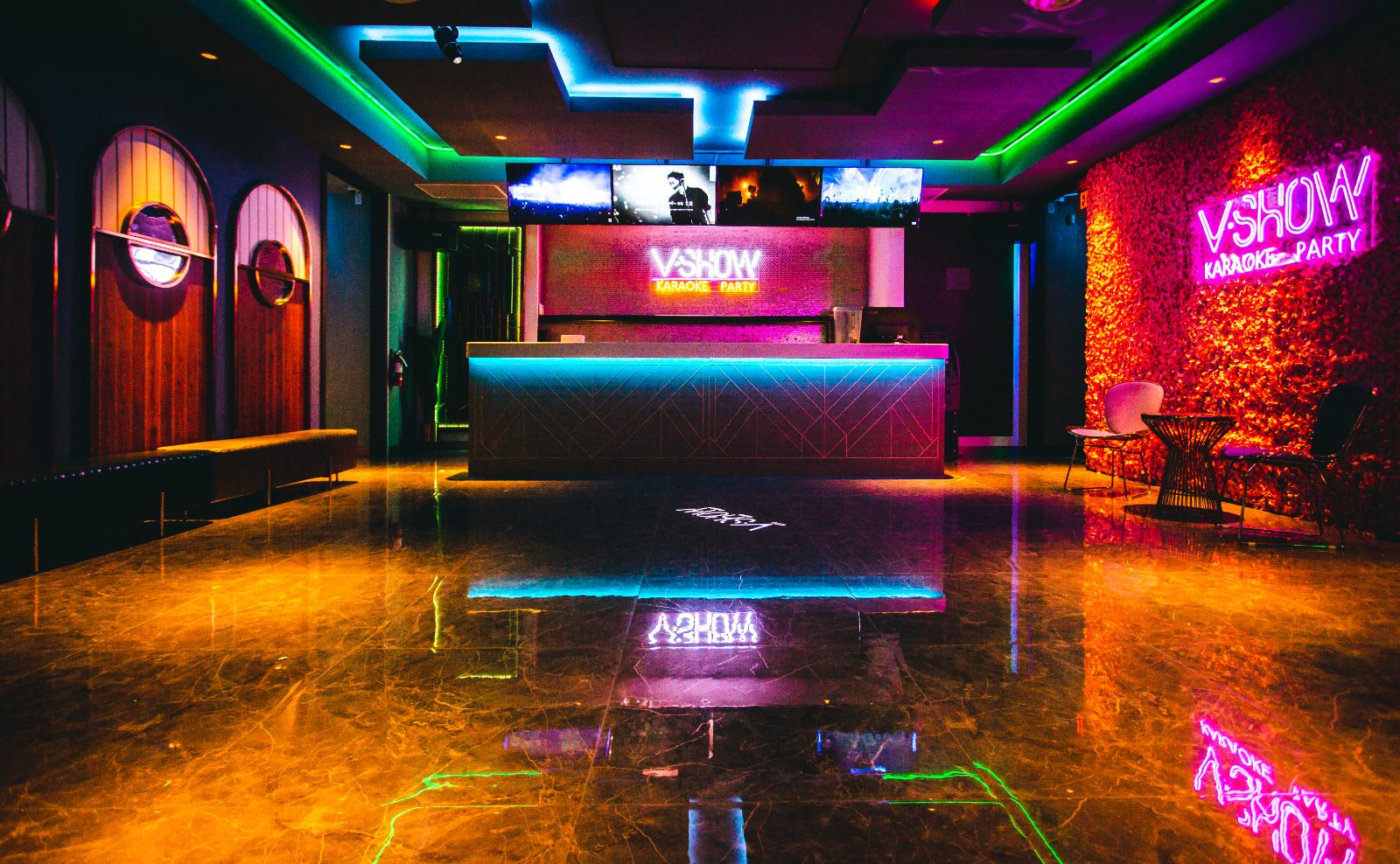 The V Show Karaoke lobby in Metrotown, with a lit reception desk, screens overhead and a red flower wall under the V Show Karaoke Party neon sign