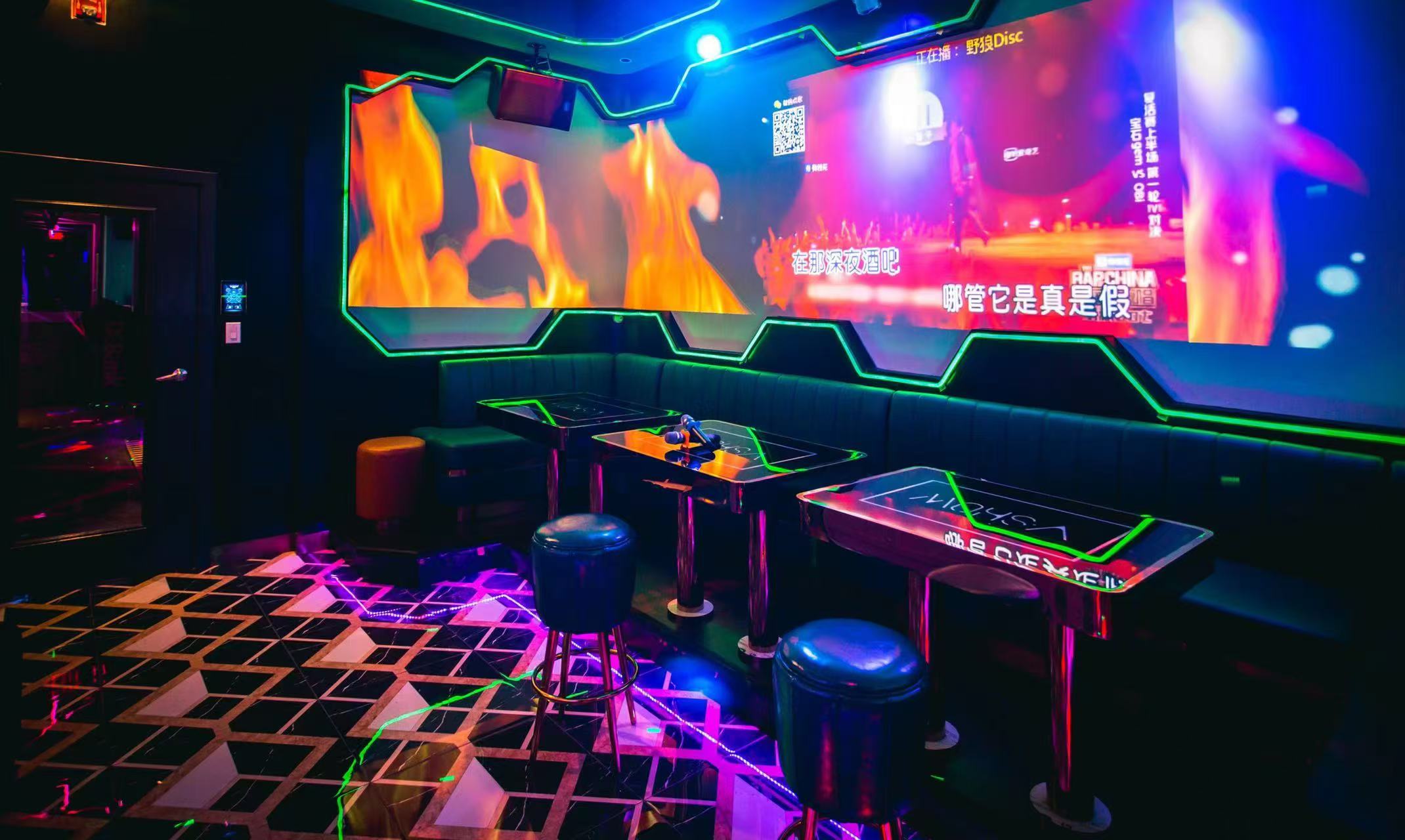 Karaoke room at V Show with a lit dance floor, neon-edged tables and a wall-wide screen