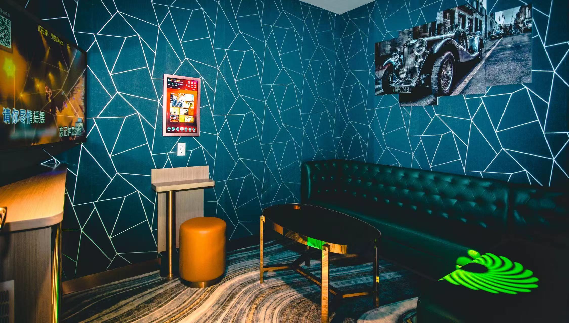 Small karaoke room at V Show with teal geometric wall panels, a green leather sofa, gold table and a wall-mounted song tablet