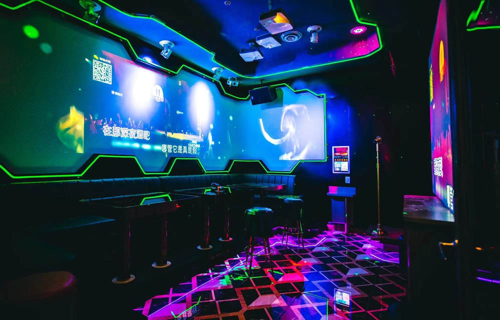 VIP karaoke room at V Show with a wall-wide screen, bar stools and a lit dance floor