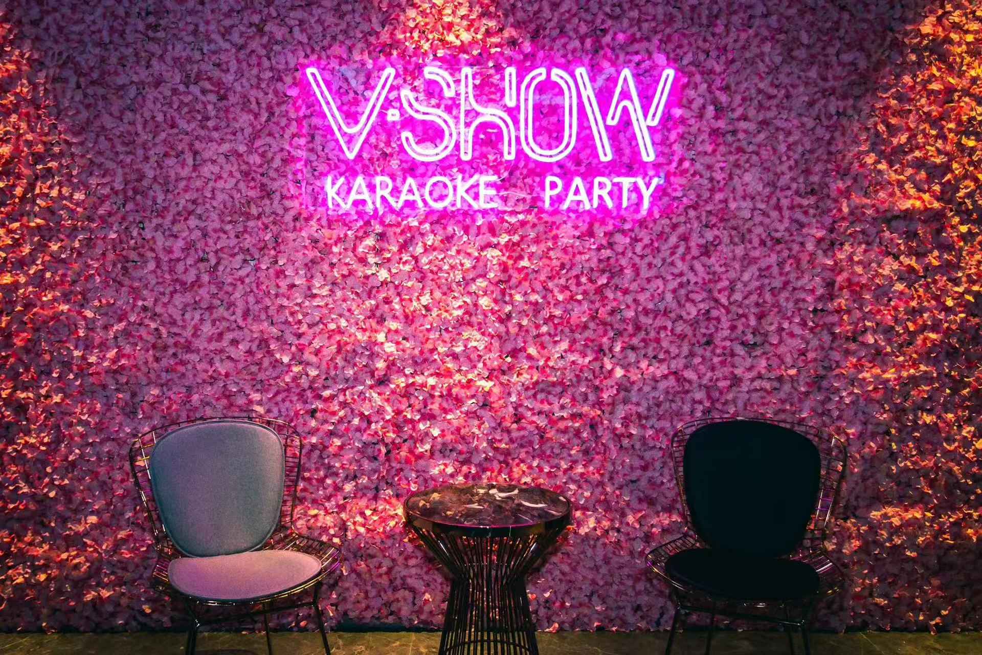 The V Show Karaoke photo wall, a pink flower wall lit by the V Show Karaoke Party neon sign with two chairs in front